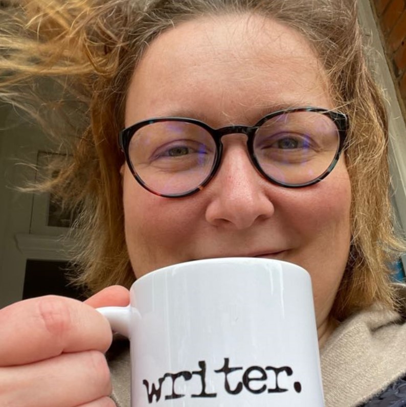 Kristina holding a white mug printed with the word writer.